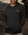 Person wearing a black hoodie with a logo in an outdoor setting