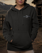 Person wearing a black hoodie with a logo in an outdoor setting